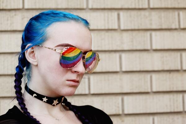Ei kvinne med blått hår og regnbogefarga solbriller