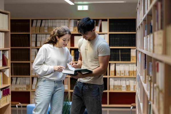 To studenter på biblioteket, ser i en bok sammen