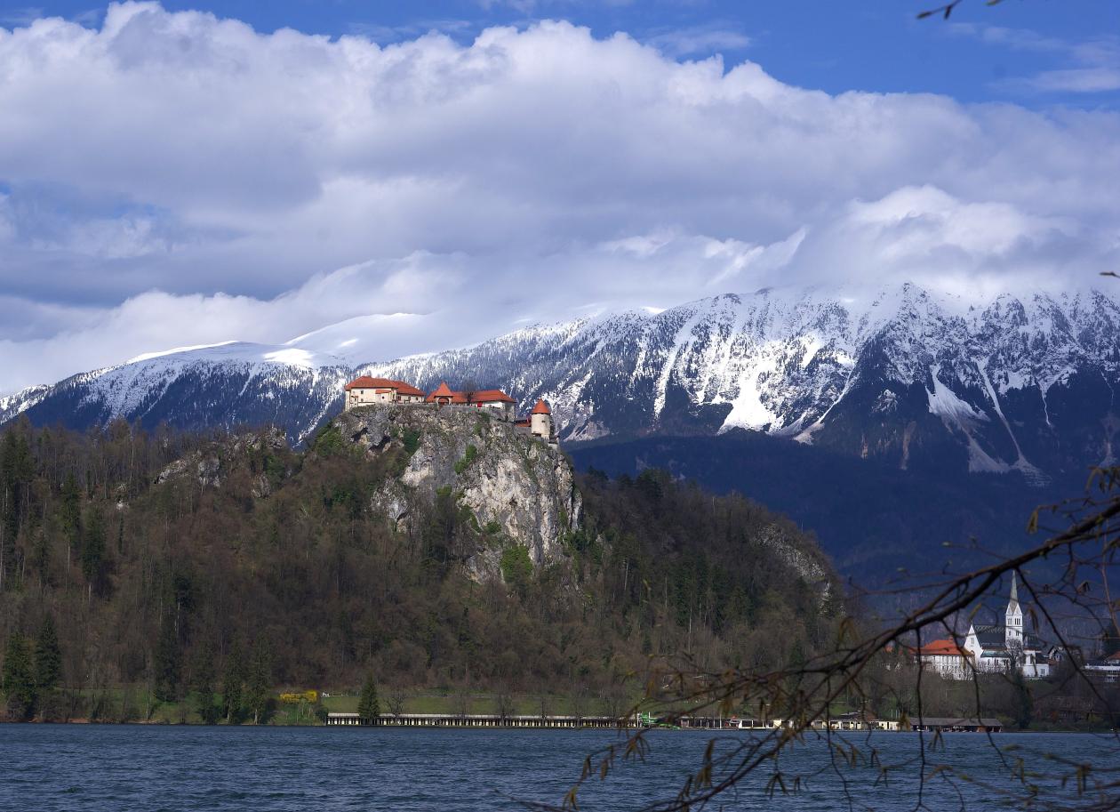 Bilde av innsjø med slott på en åskam og fjell i bakgrunnen.
