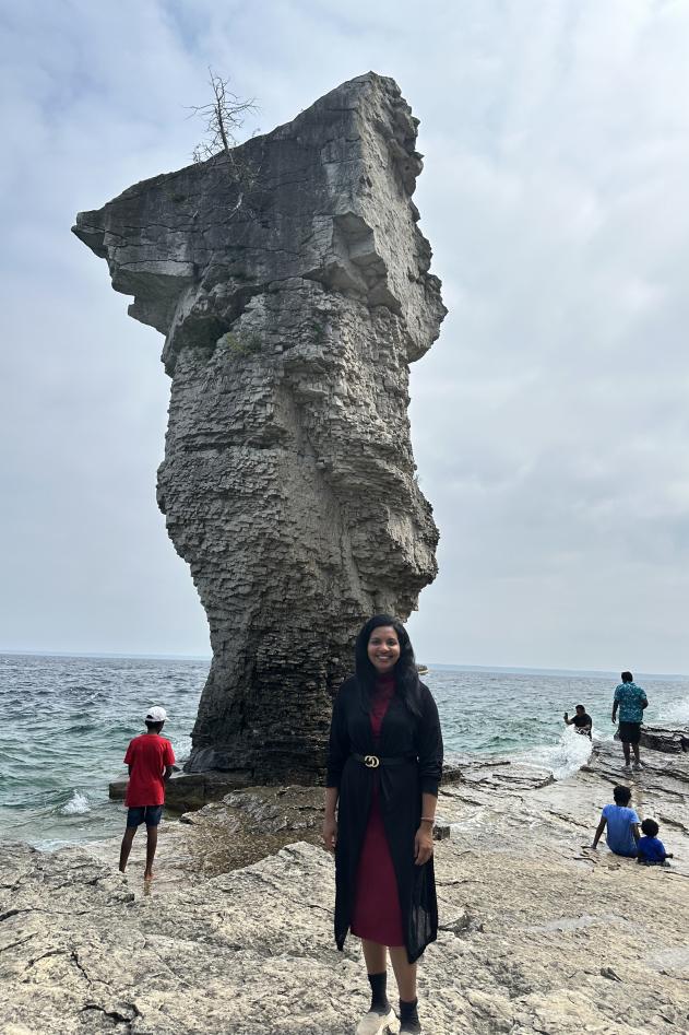 Young woman standing at the coast with rock formation behind