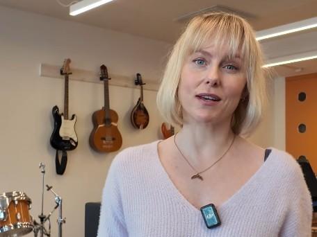 Ingrid Bolsø Berdal snakker til kanera i et rom med musikkinstrument i bakgrunnen