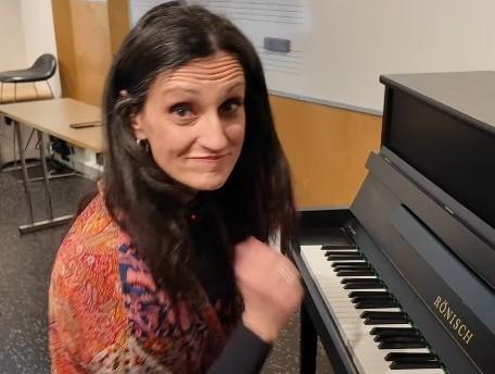 Jelena Golubovic sitter ved pianoet, snakker og gestikulerer foran kamera