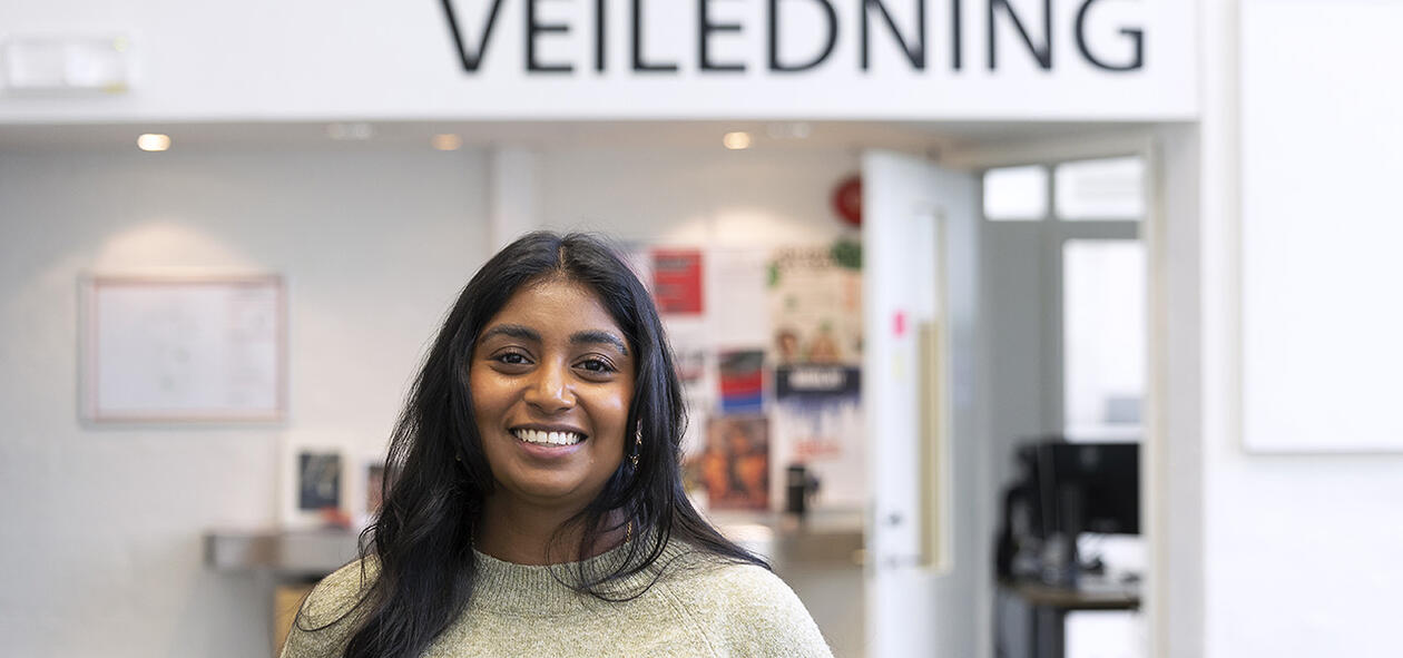 Smilende veileder Medhusja skilt med ordet veiledning i bakgrunnen