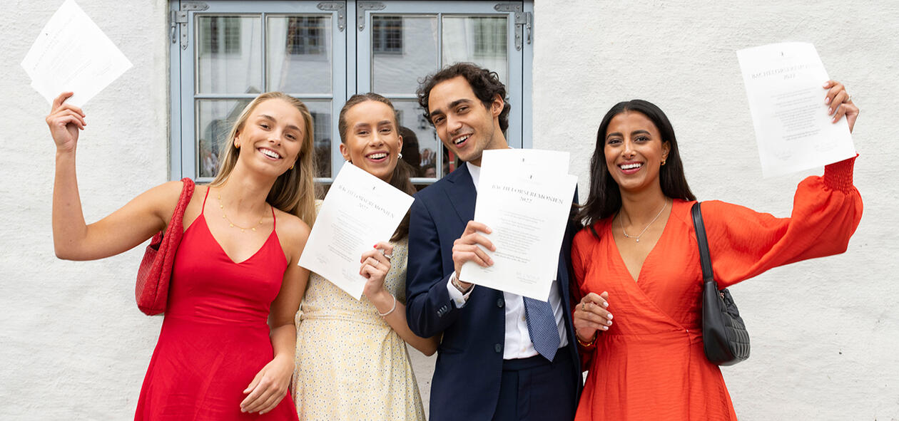 Glade bachelorstudenter som holder sitt vitnemål frem.