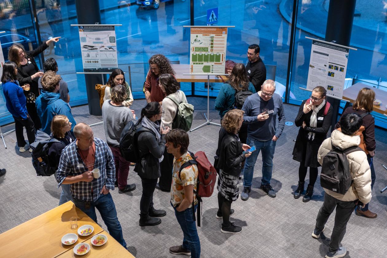 Image taken from above showing a group of conference participants engaged in conversation with 3 of the conference posters in the background