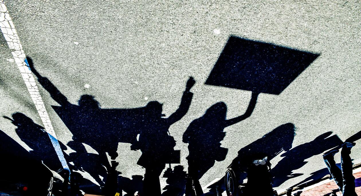 Shadows on the asphalt of people holding signs
