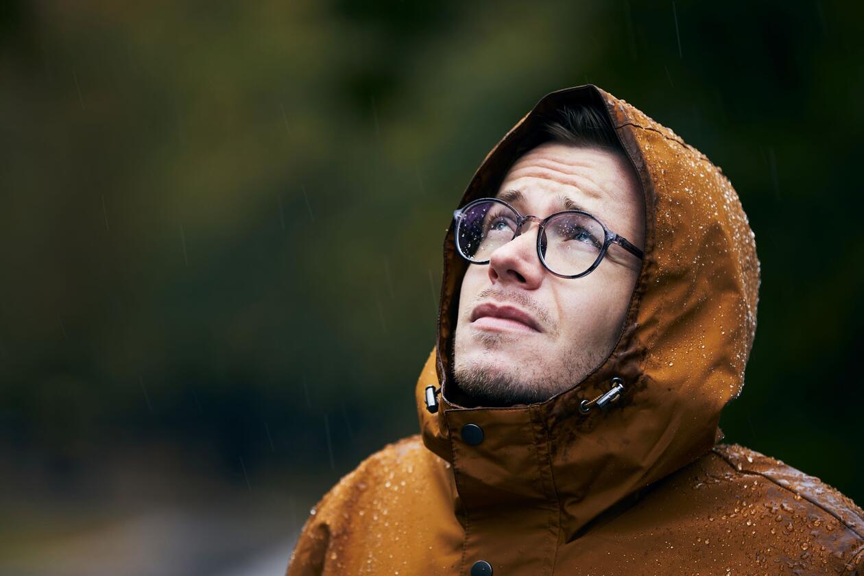 Mann i regn ser bekymret opp mot himmelen