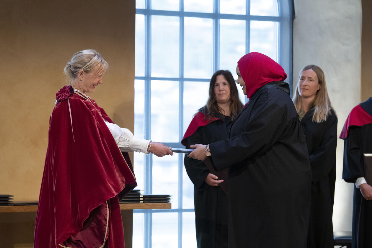 Bilde av ny doktor som får diplom av rektor på scenen i Universitetsaulaen 