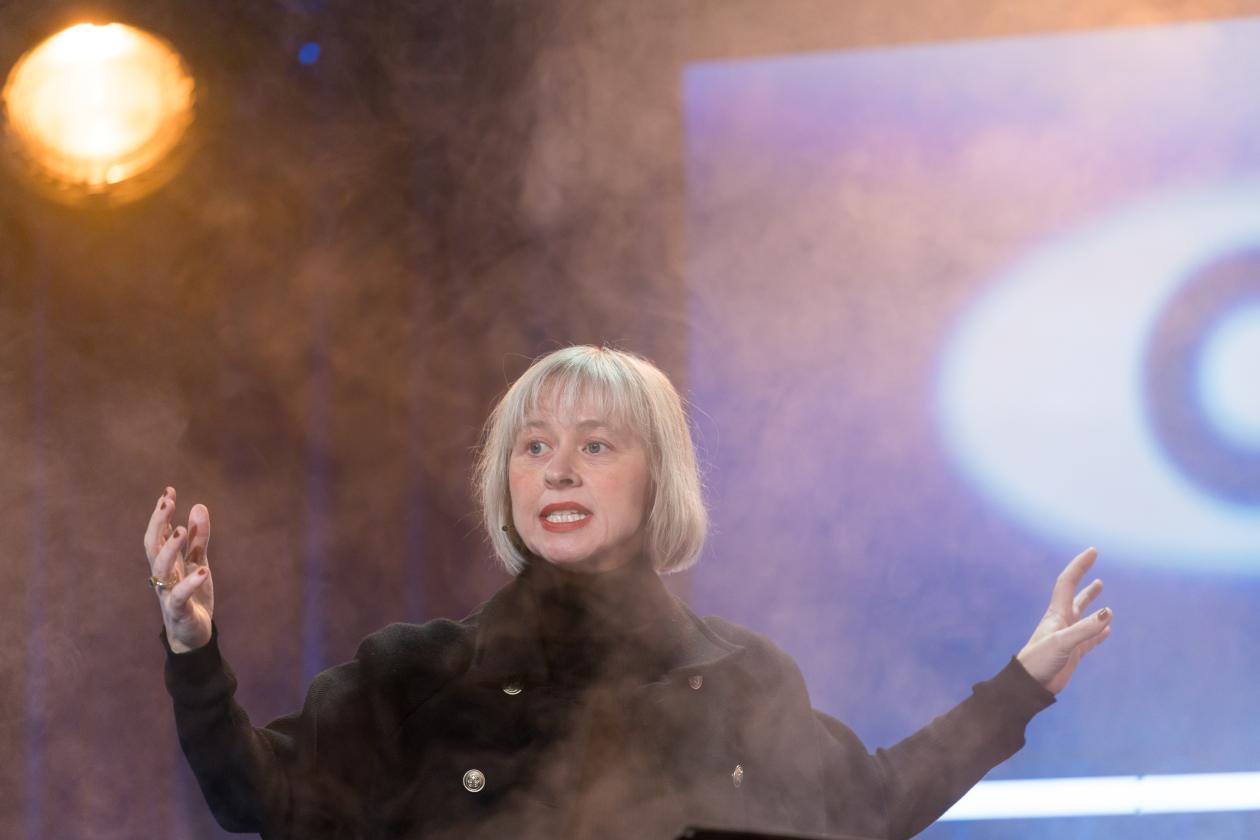 Kvinne på scenen, omringet av røyk og dyster stemning. Vi skimter et øye i bakgrunnen.