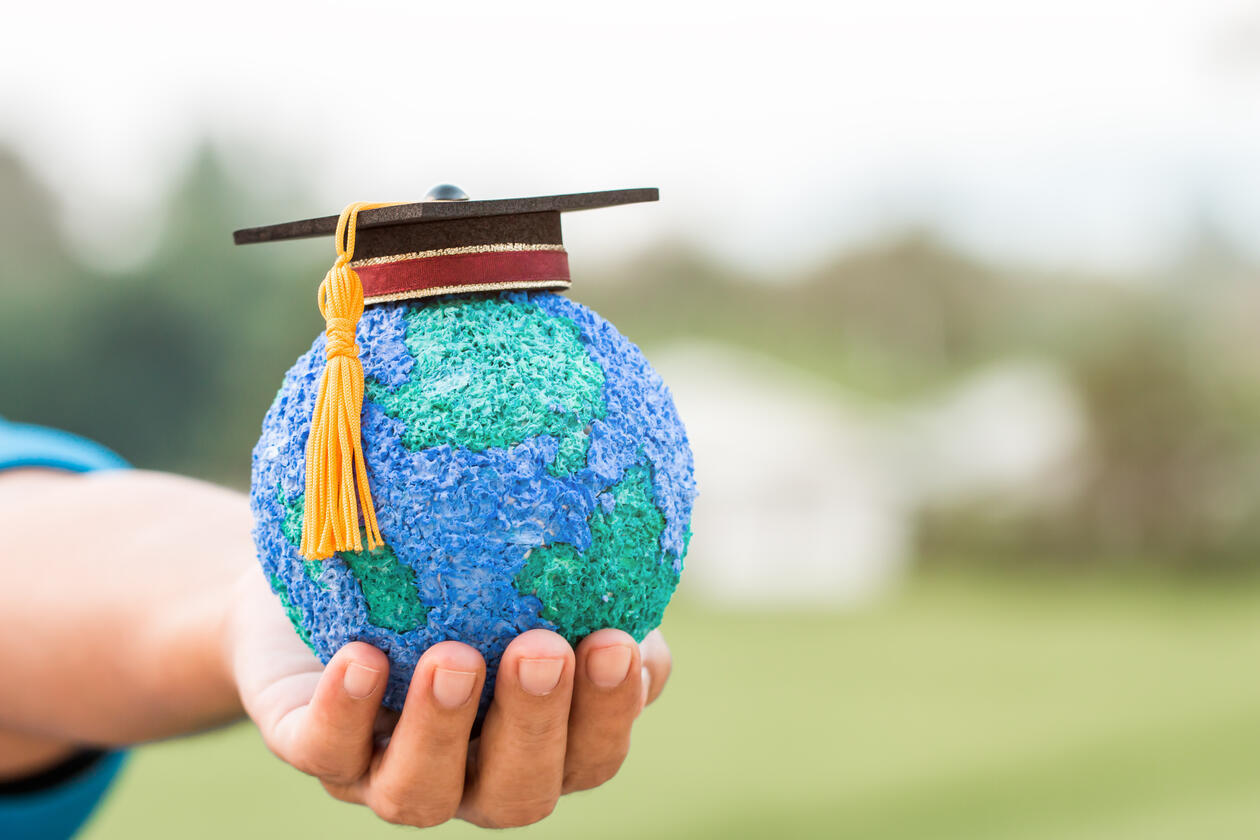 A hand holding a globe with an academic cap