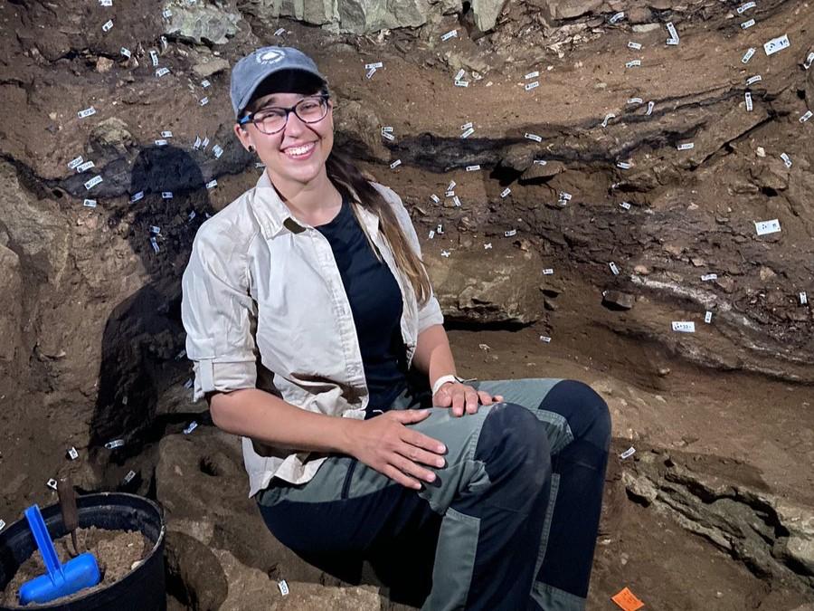 Image of Asia Alsgaard holds a Ph.D. in anthropology, specializing in identifying animal skeletal remains, or zooarchaeology sat in Blombos Cave South Africa, doing fieldwork looking at the photographer.