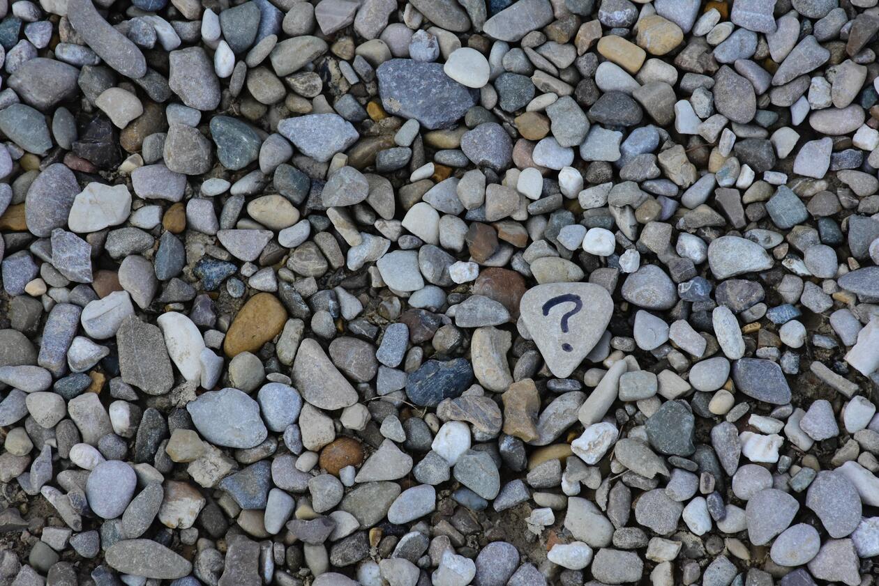 Many small pebbles in various colours, one large pebble has a question mark on it