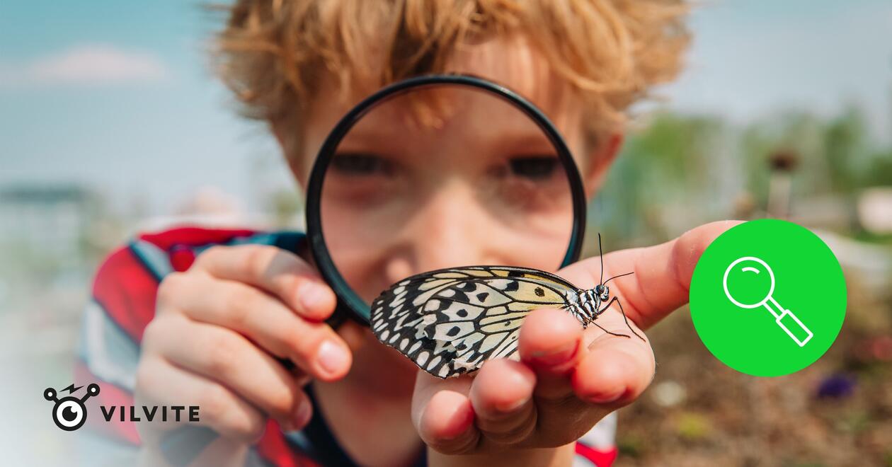 A child looking at a butterfly through a magnifying glass, Vilvite's logo and a green circle with a magnifying glass to the right of the child