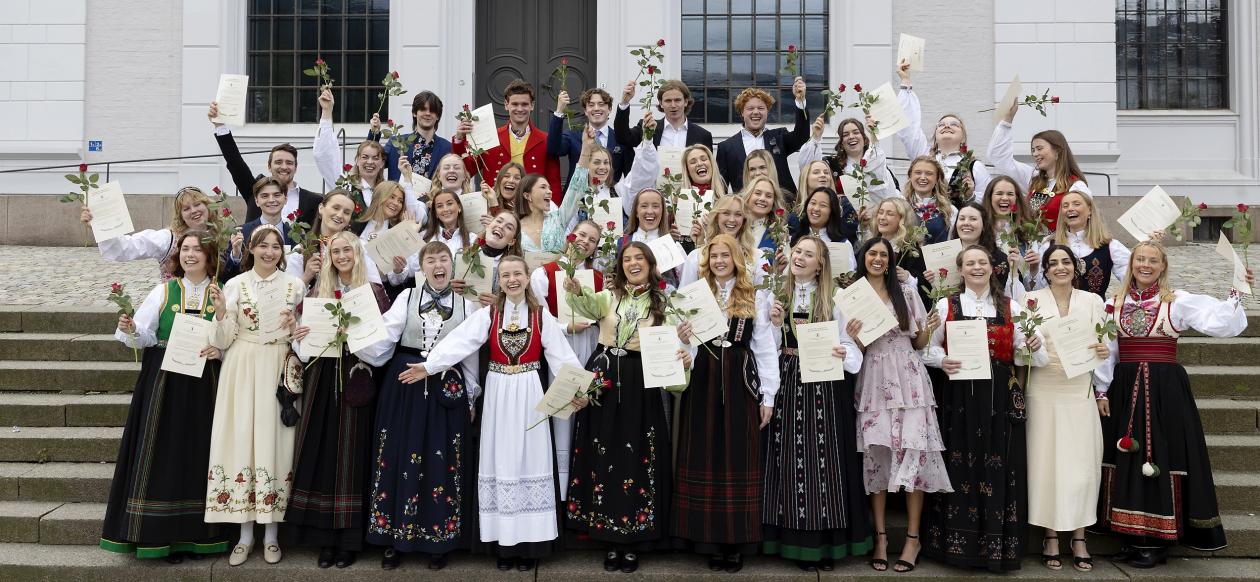 Studenter på avslutningsseremoni med diplom og roser i hendene
