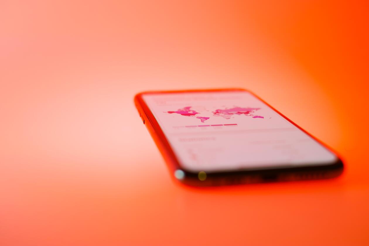 Photo of a mobile phone on a red background, indicating infection rates for the COVID-19 pandemic.