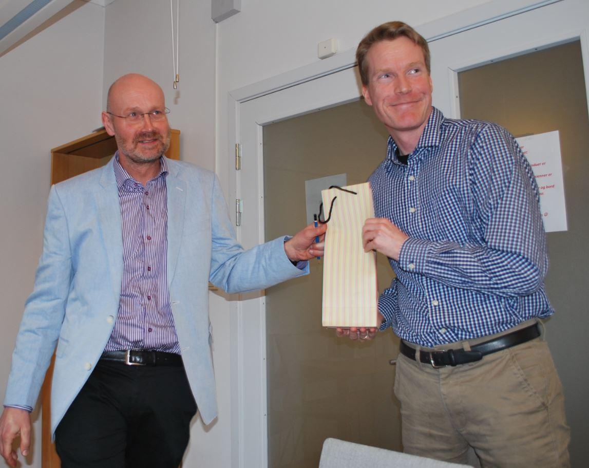 Instituttleder Jan Heiret, t.v., overrekker en vinflaske til Eivind Heldaas Seland, som oppnådde flest publikasjonspoeng av instituttets forskere i 2016.
