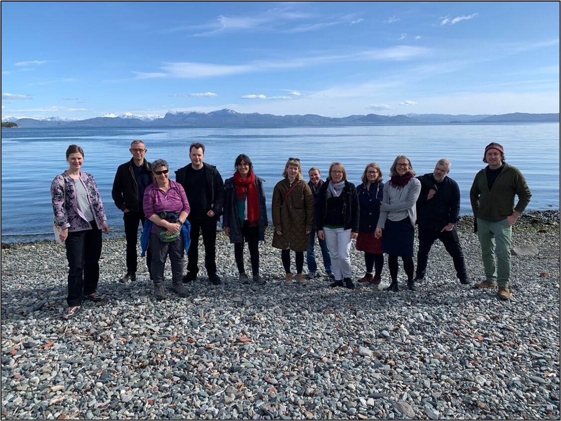 A group of people posing on a pebble beach, blue sea and sky in the background