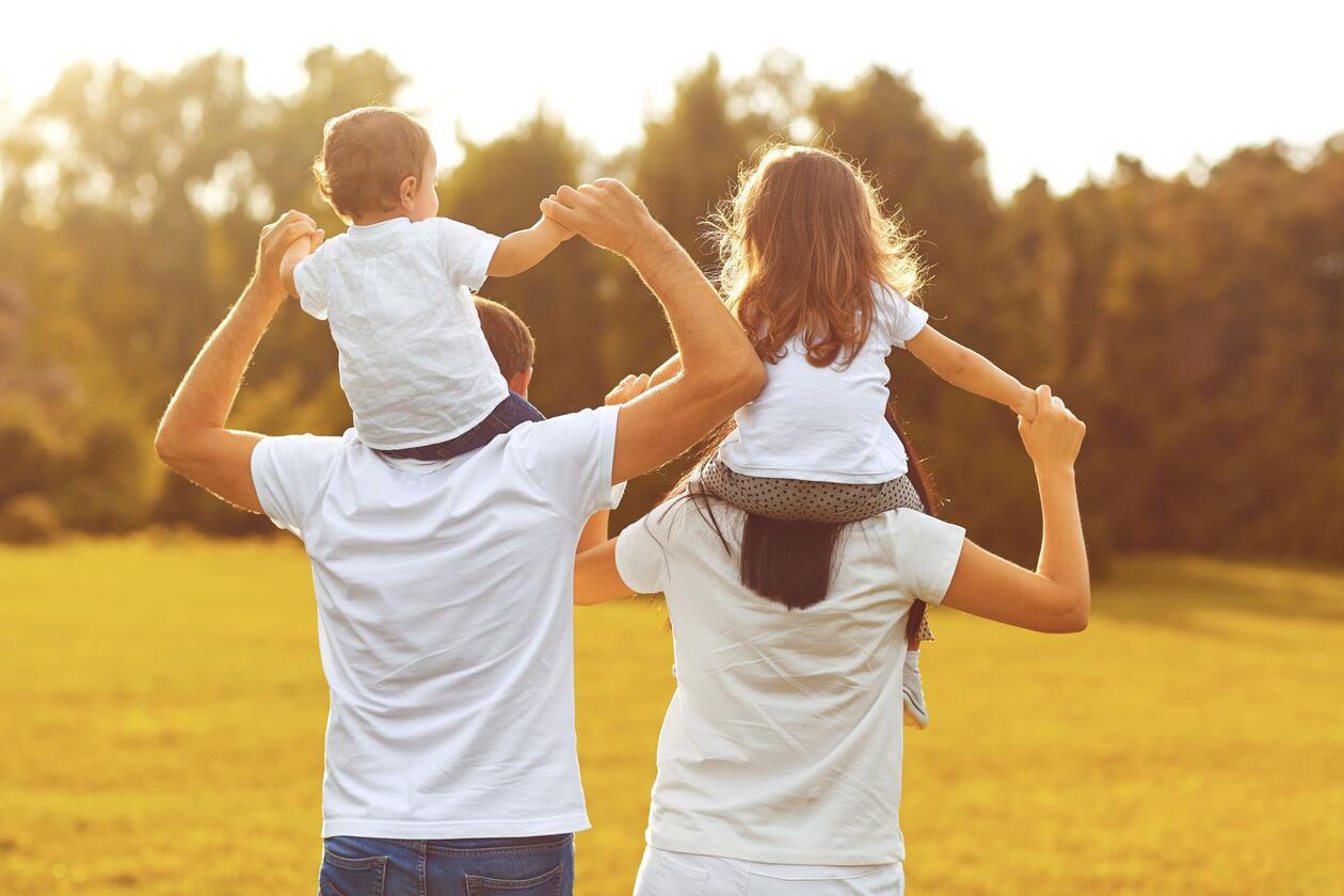 Family of four seen from behind. Children on top of parent's shoulders