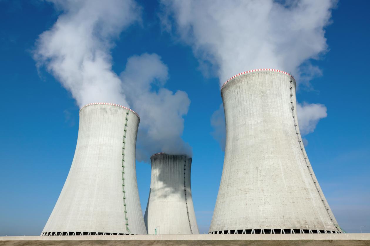 Illustration photo showing 3 industrial chimneys releasing white smoke towards the blue sky at a nuclear power plant