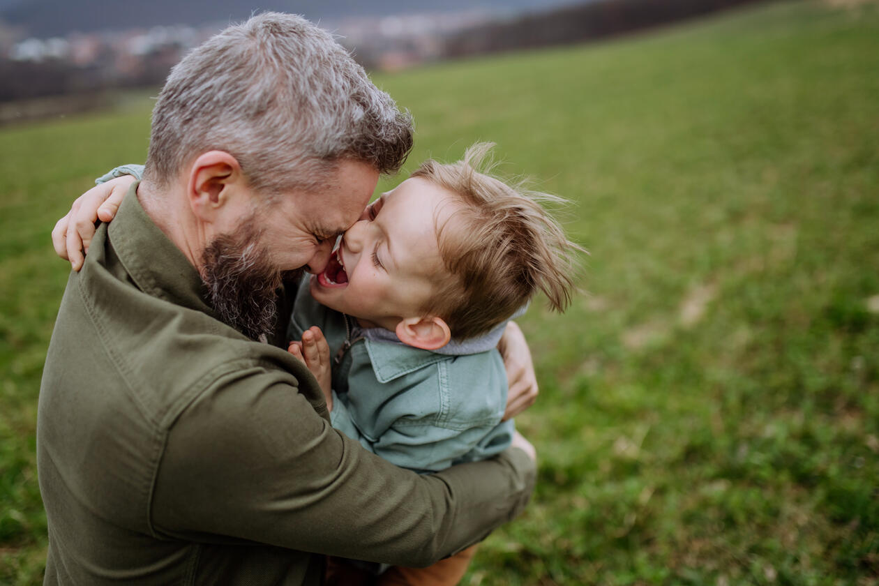 bilde av en mann som holder en gutt som holder på å lekent bite han i nesa 