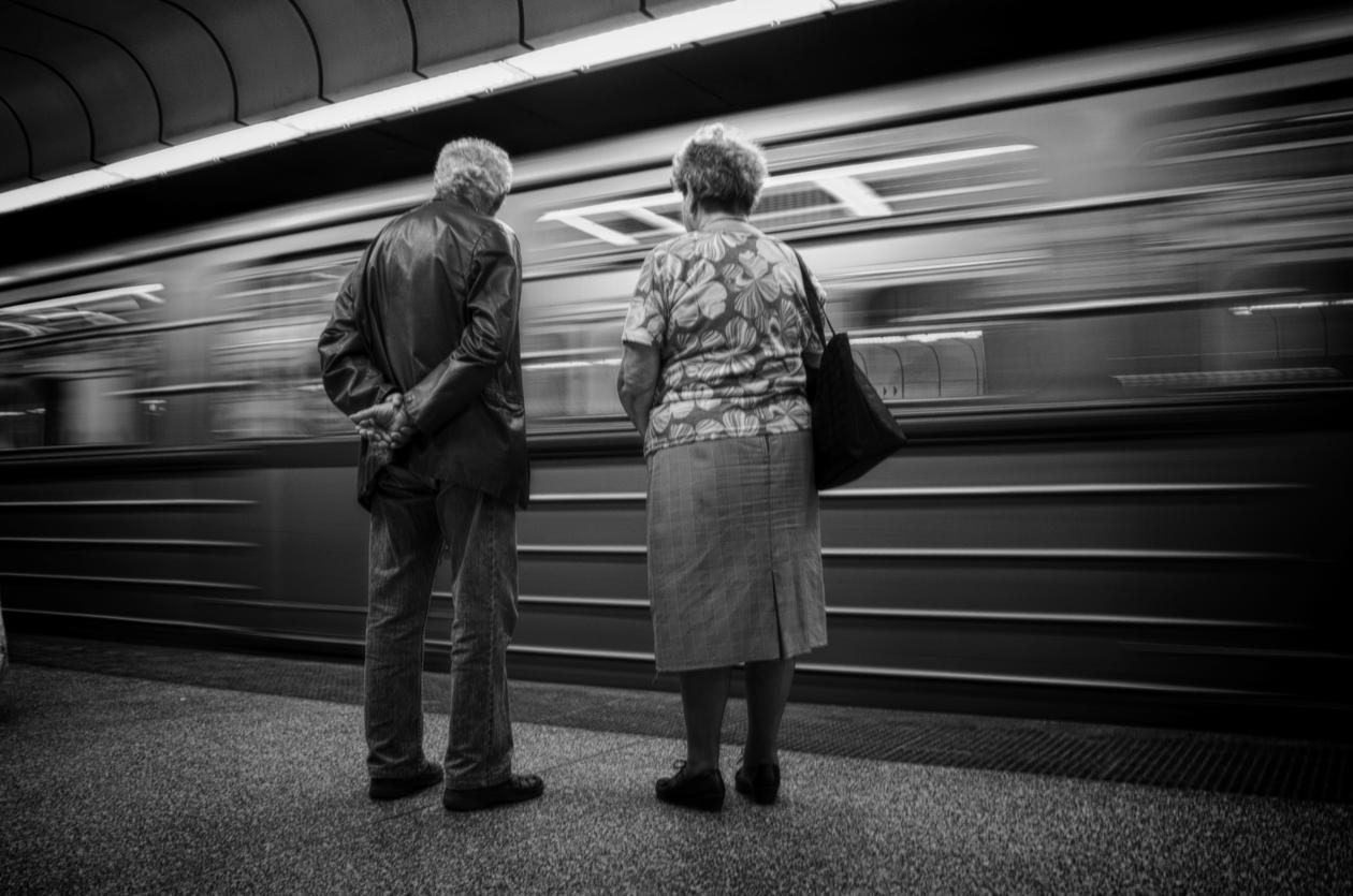 Et eldre par står på en perrong og et tog suser forbi