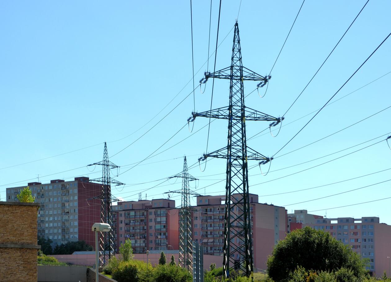 Photo showing power poles in front of a few blocks of flats under a blue sky.