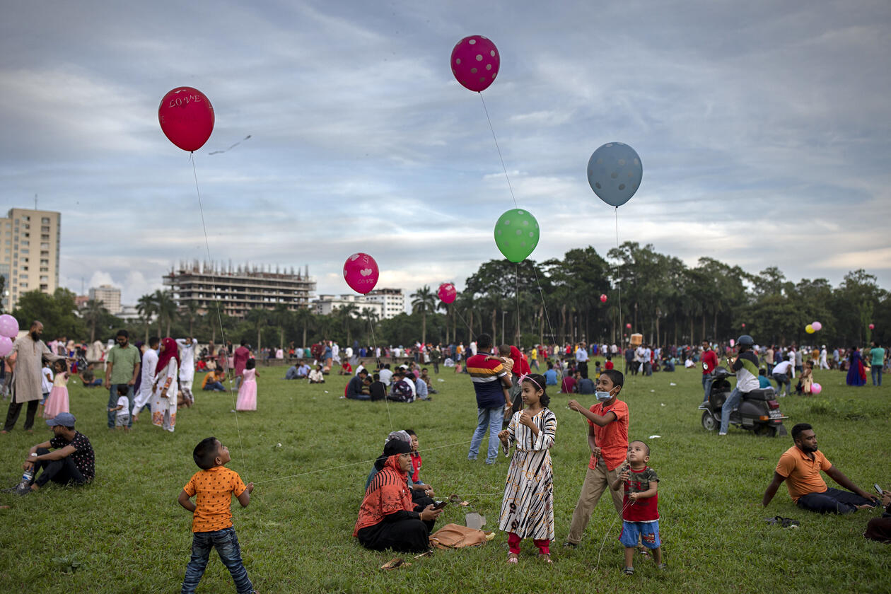 Children play with balloons in a park Dhaka, Bangladesh. Green grass and red, blue, green and pink balloons floating upwards. 