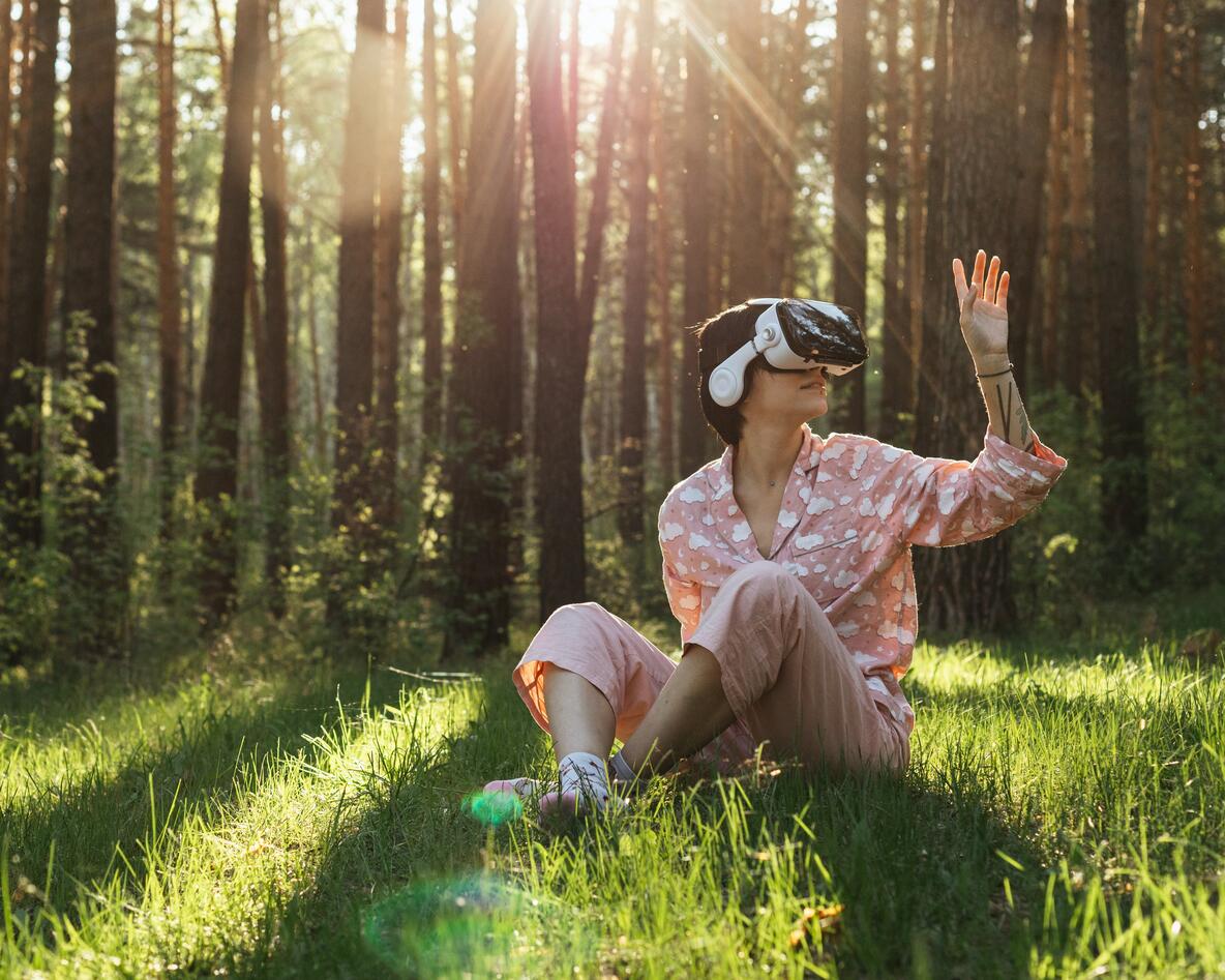 Person sitting on the ground in a forest with VR glasses on