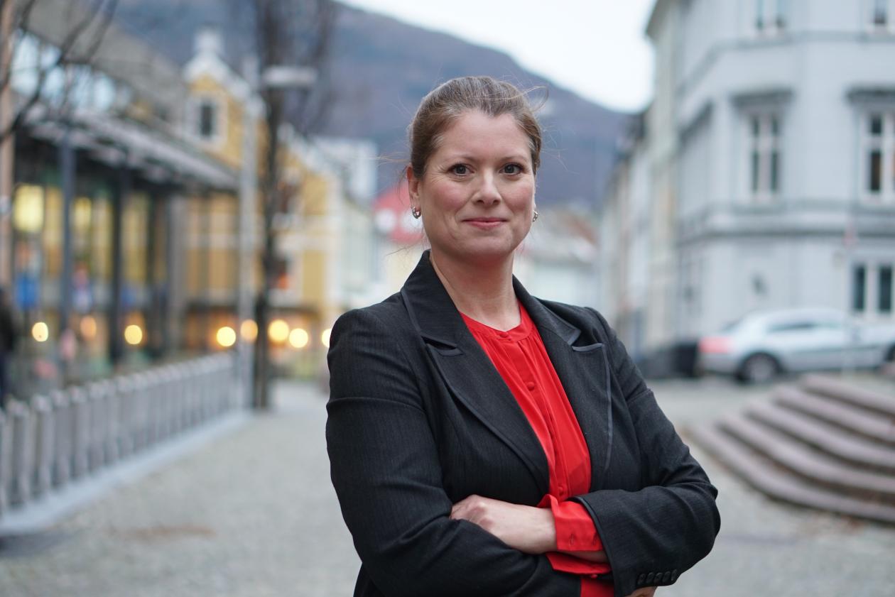 Bilde av Strønen med rød topp og svart blazer foran Bergens-landskap