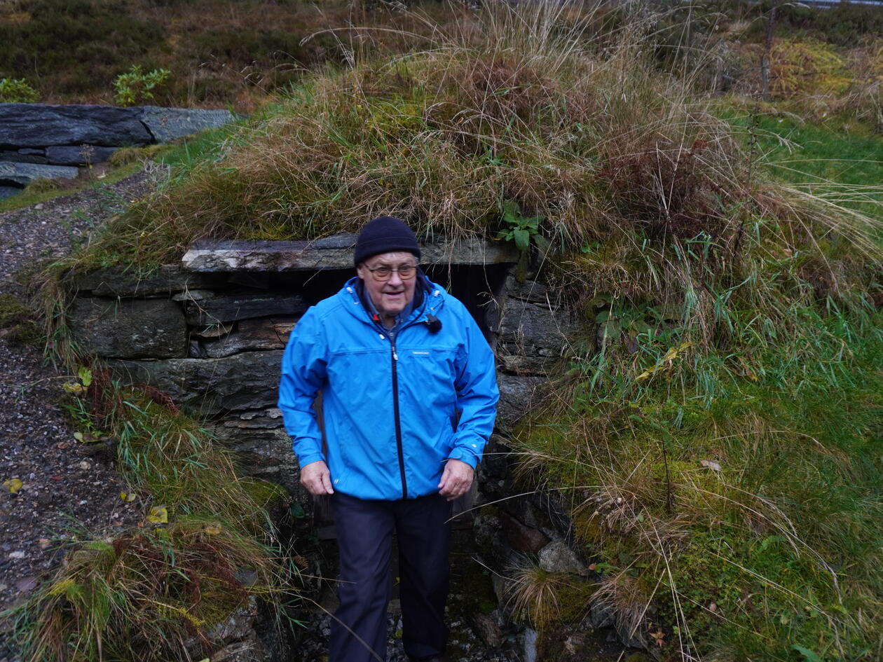 Erling Kleiveland i blå regnjakke stående foran en gammel potetkjeller