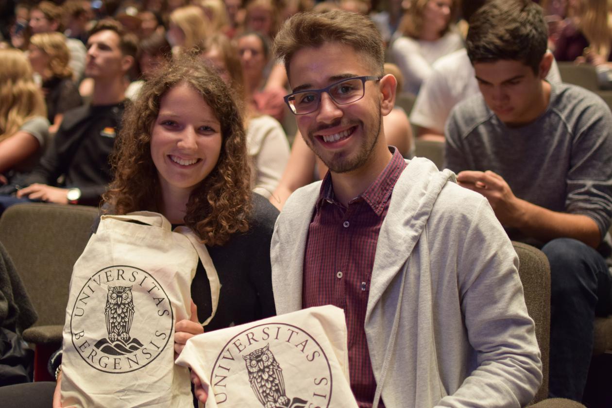 Two students smiling, facing the camera, holding a UiB tote bag