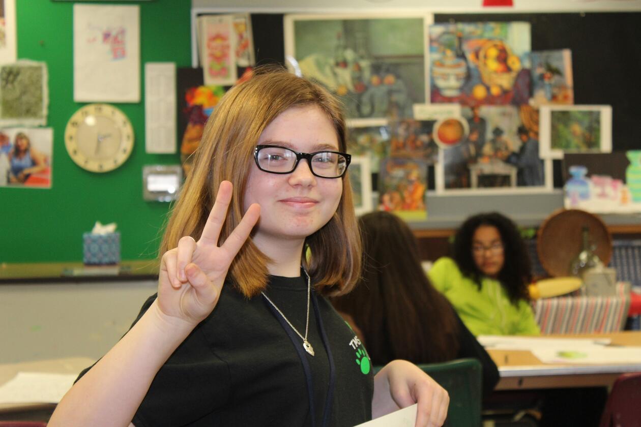 Female pupil in classroom showing V-sign