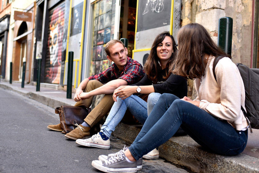 Tre studenter sitter på fortauskanten i en gate i Frankrike