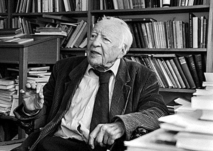 Sort-hvitt bilde av Hans Georg Gadamer sittende med en stabel bøker rundt seg.