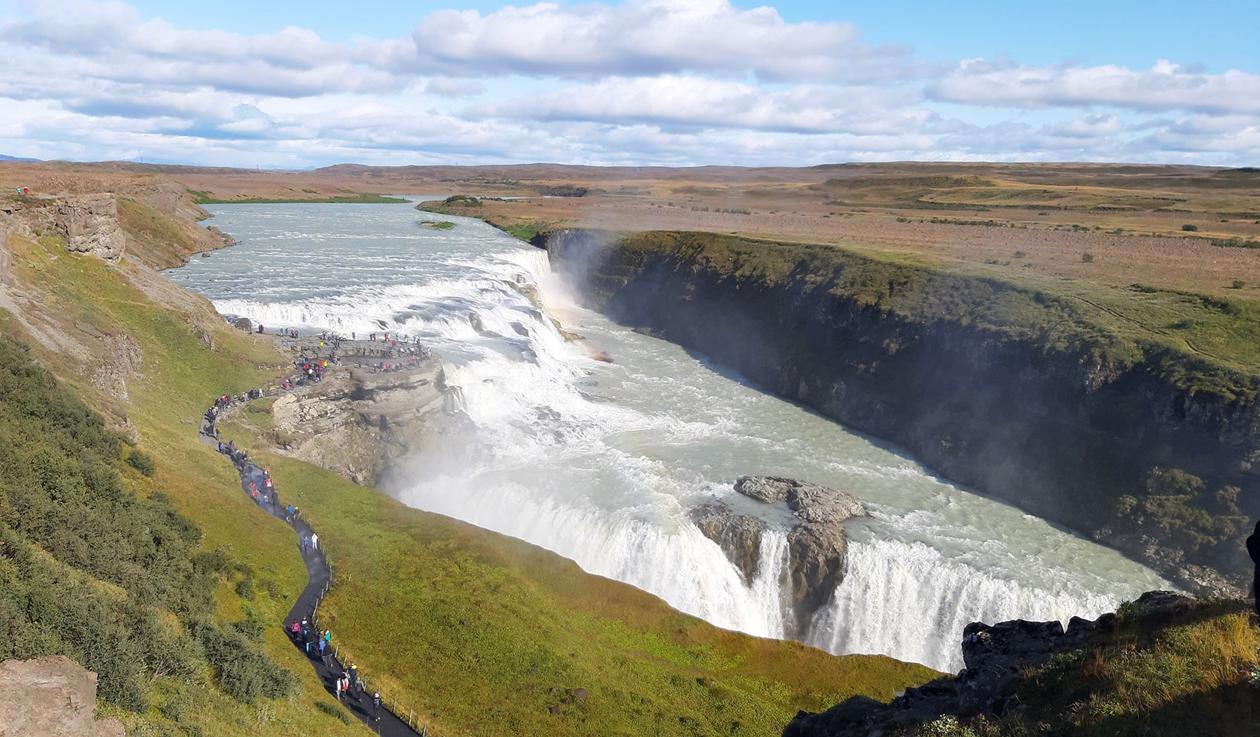 Gigantic waterfall at Iceland, and people walking into a view plateau in the middle of it.