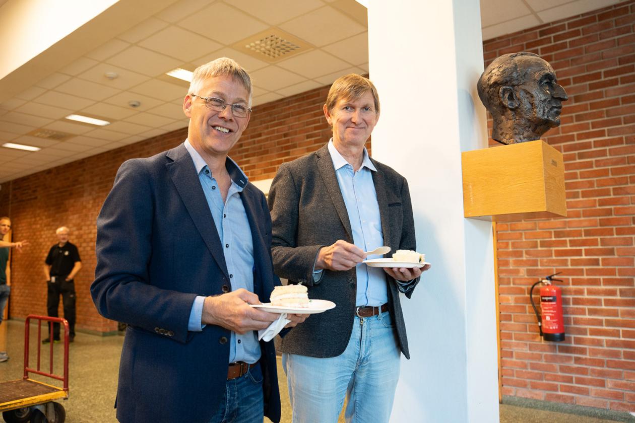 Instituttleder Kjetil Ullaland og prodekan Øyvind Frette med hvert sitt kakestykke ved bysten til Bjørn Trumpy.
