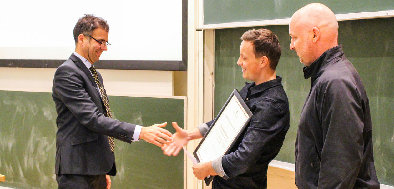 To smilende menn mottar et diplom fra visedekan for utdanning i Stort auditorium.