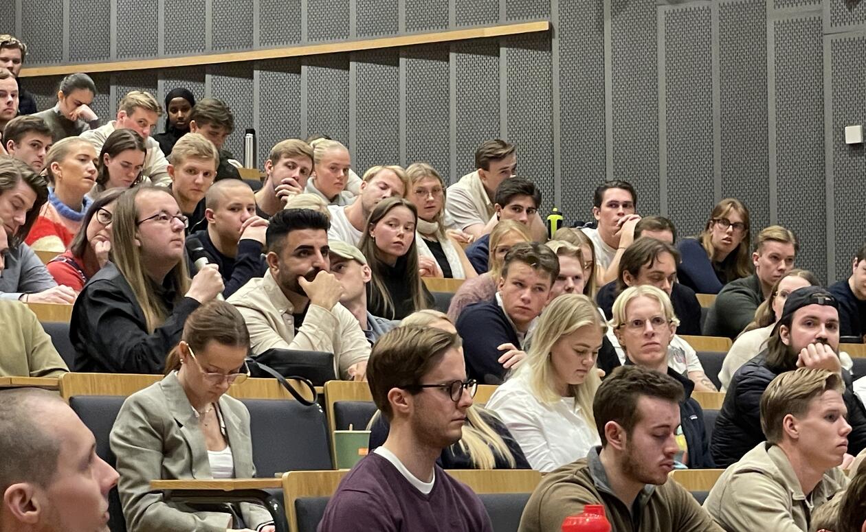 Nærbilde av studenter i salen. Noen av dem stiller spørsmål