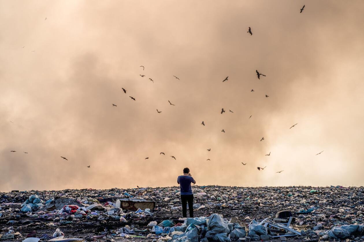 Man stands in pile of plastic litter and takes a photo