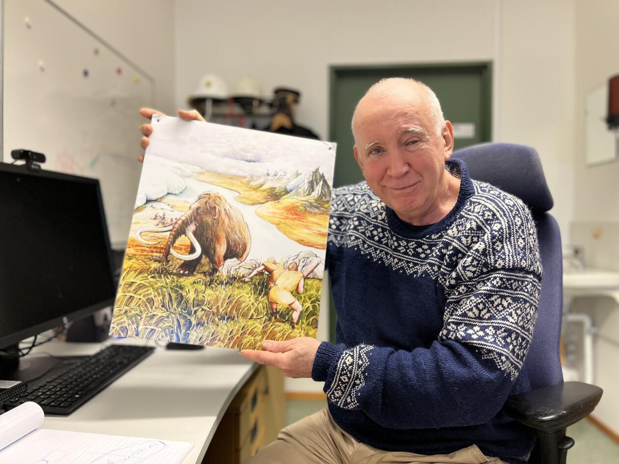 John Inge Svendsen på kontoret sitt som holder opp et bilde av en Mammut. 