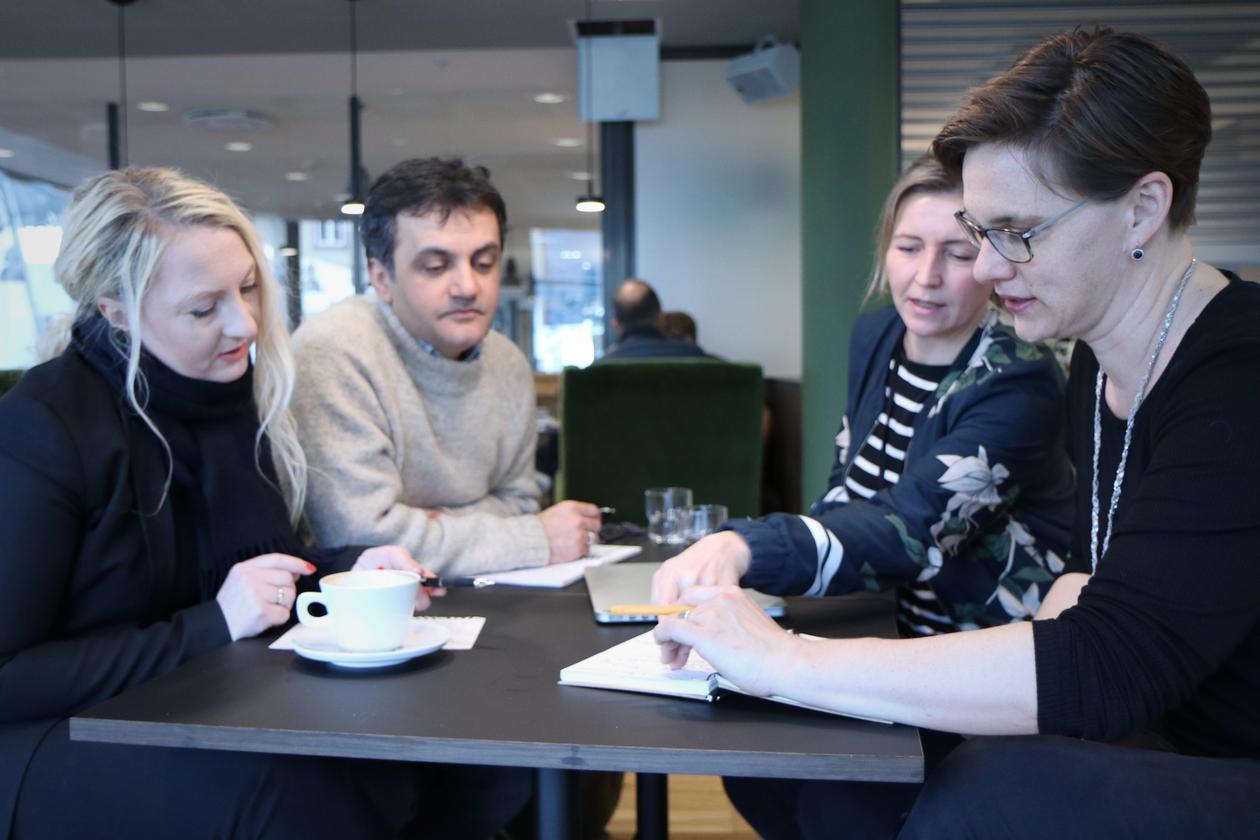 Fire personer med kaffekopper sitter ved et bord og diskuterer.