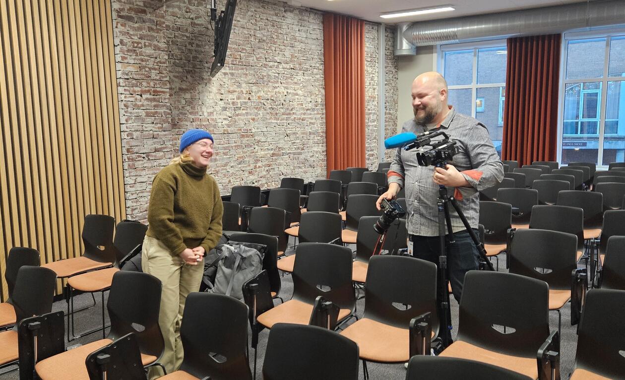 En kvinne blir intervjuet av en mann i et klasserom.