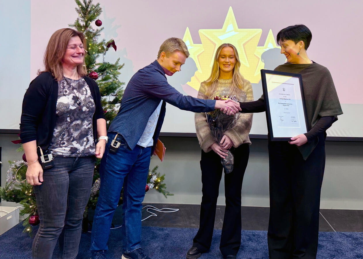 Bildet viser to personer som får overrakt blomster og diplom på 100 000 kr.