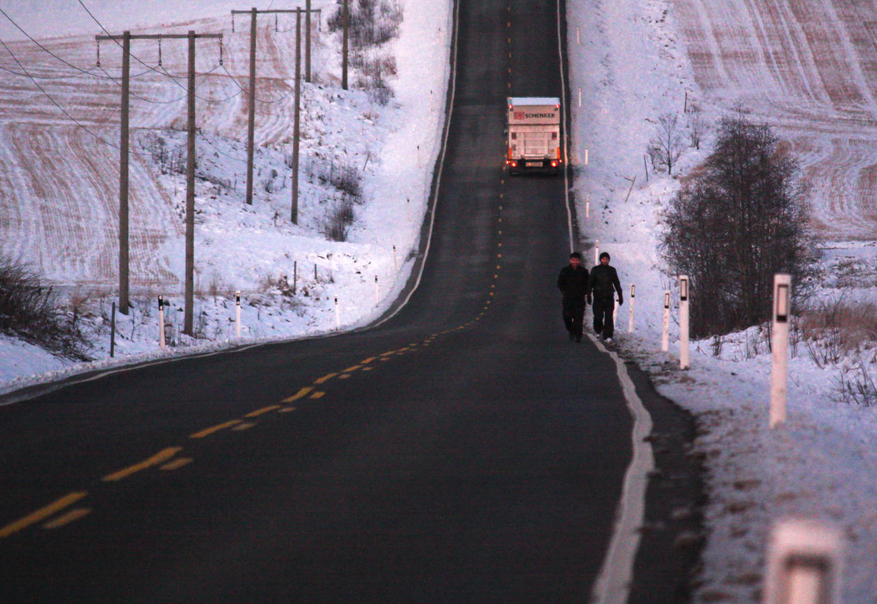 Aviste asylsøkere går langs en landevei på vinterstid
