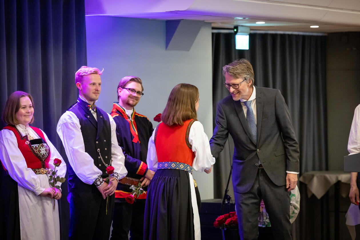 Studine i bunad får rose av mann i dress