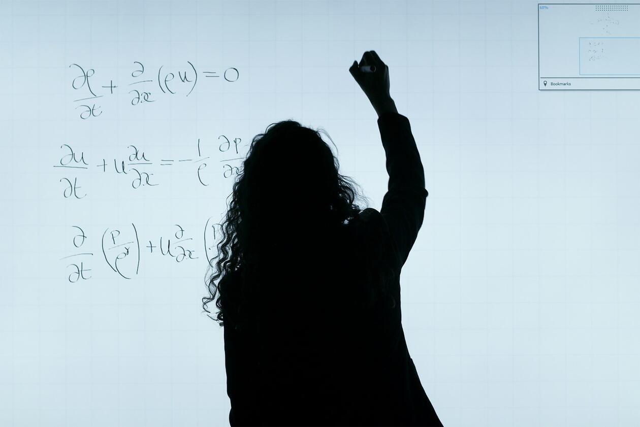 Woman writing mathematical formulas on a white board