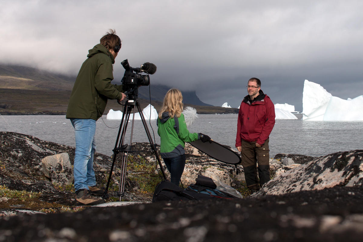 To personer filmer mann som står foran havet med isbreer i bakgrunnen