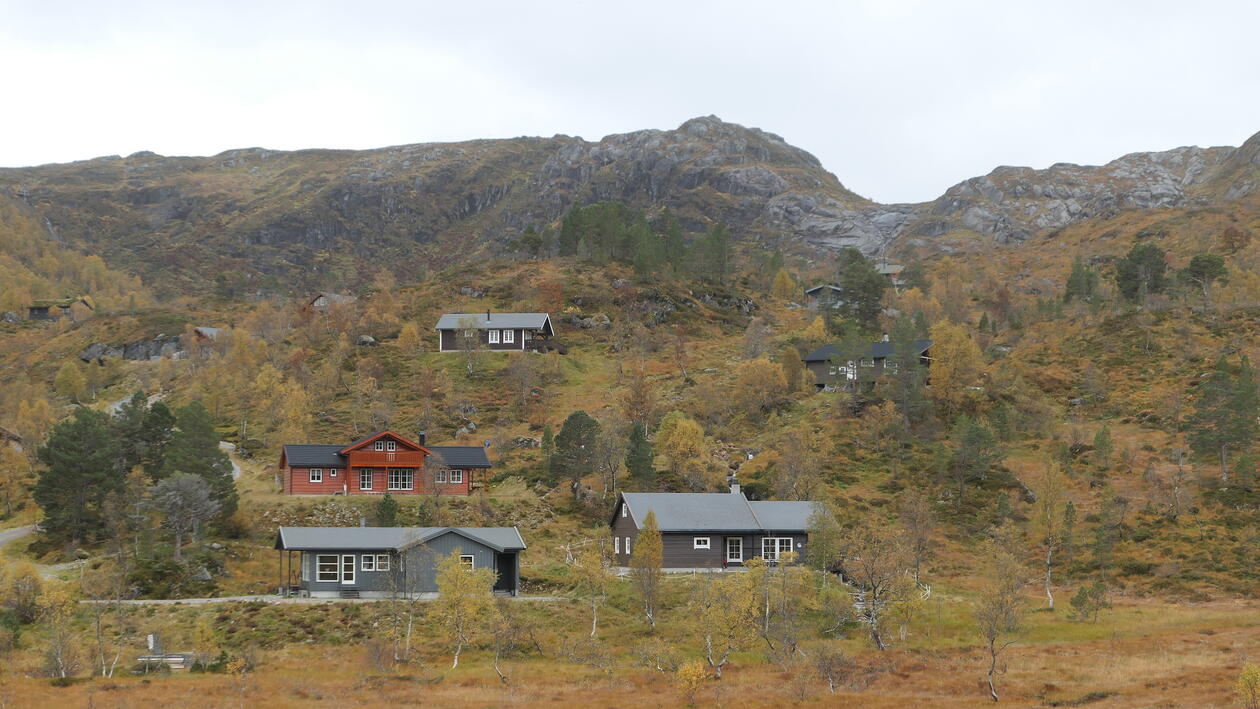 Hytter i et høstlig fjellandskap med fjelltopper i bakgrunnen.