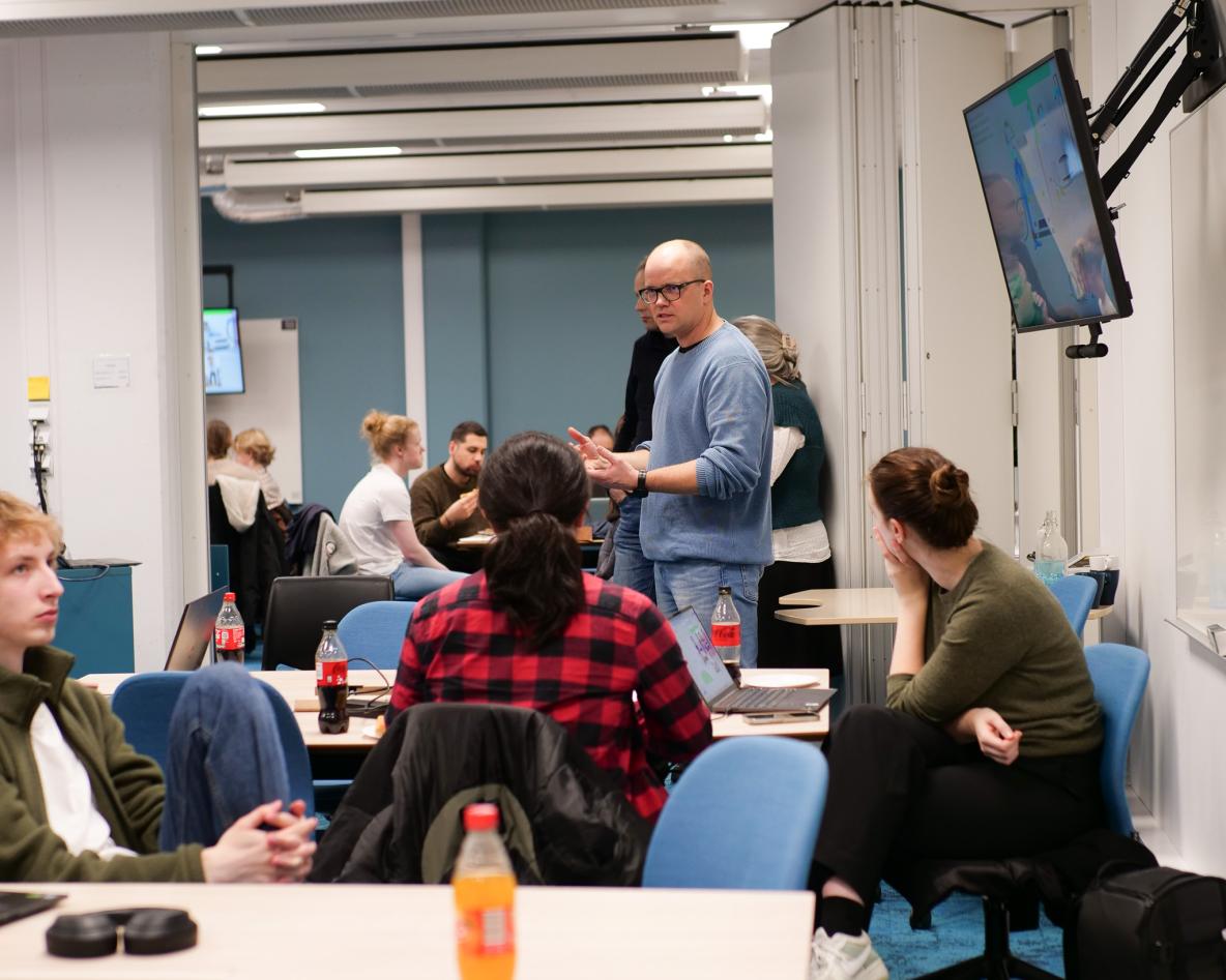 Mann snakker til forsamling av studenter som sitter på et aktivitetsrom