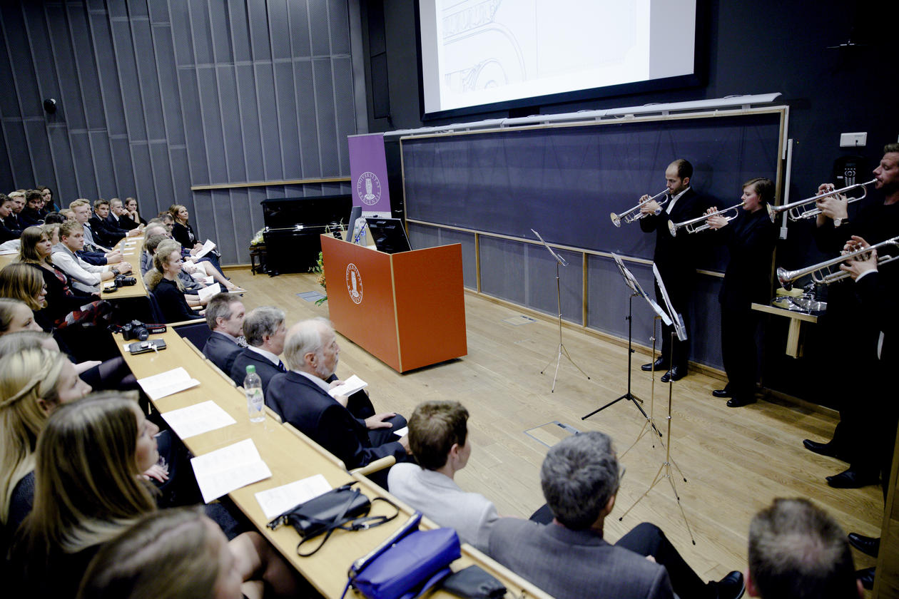 Fire trompetister spiller foran et fullsatt auditorium